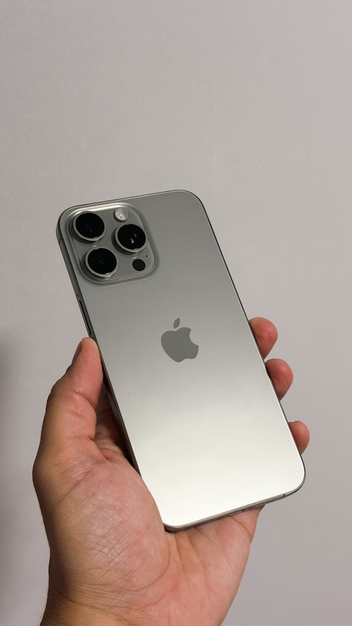 Hand holding a sleek, silver smartphone with multiple rear cameras in focus.